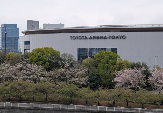 Toyota Arena Tokyo exterior with clear name signage above cherry trees beside the waterway in Aomi, Tokyo