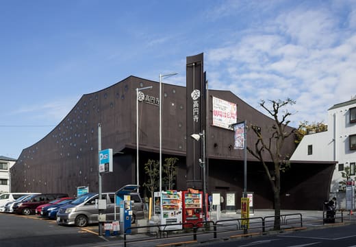 Dark curved facade of Za-Koenji public theater with vertical sign and vending machines in Suginami, Tokyo