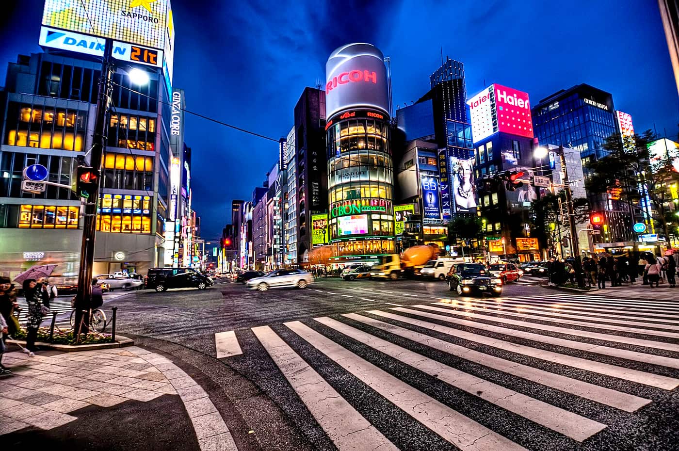 Neon-lit department stores around a wide Ginza crossing at night