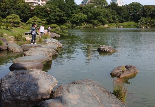 Visitors crossing the stepping-stone path over the pond in Kiyosumi Gardens