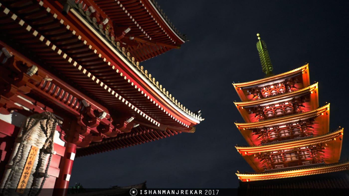 Senso-ji five-storey pagoda glowing red at night beside the Hozomon gate roof