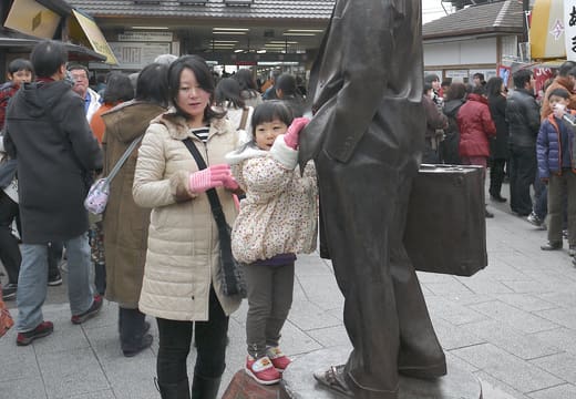 Bronze Tora-san statue outside Shibamata Station with visitors posing beside it