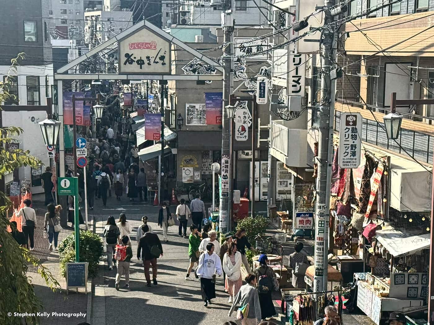 Shoppers browsing food stalls under the entrance sign of the Yanaka Ginza shotengai