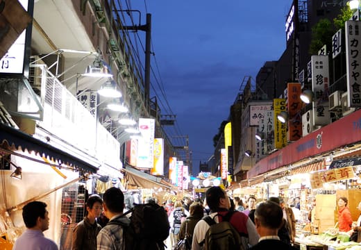 Shoppers walking the Ameya-yokocho market lane at dusk beneath hanging signs, Ueno