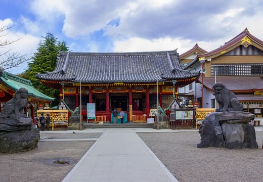 Worship hall of Asakusa Shrine flanked by stone komainu guardians under a blue sky
