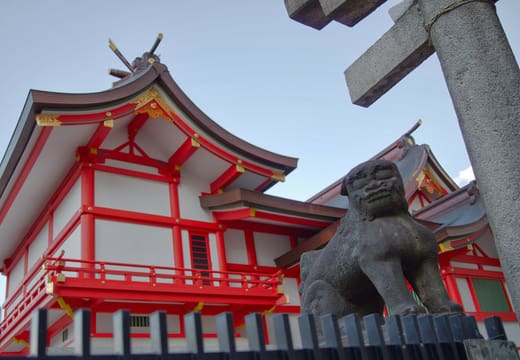 Vermilion and white worship hall of Hanazono Shrine with a stone komainu in front
