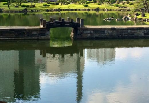 Stone bridge and pines mirrored in the pond of Kyu Shiba Rikyu Gardens