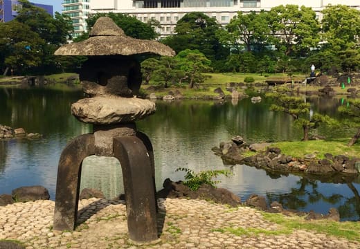 Rustic stone lantern on a pebble shore by the pond in Kyu Shiba Rikyu Gardens