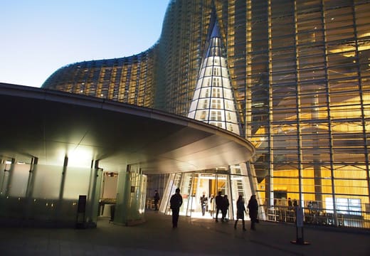 Wavy glass facade and cone entrance of the National Art Center Tokyo glowing at dusk