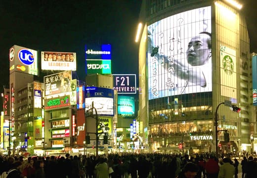 Crowds waiting at Shibuya Crossing at night under giant video screens and neon signs