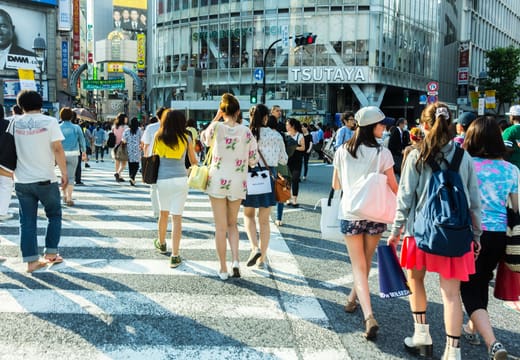 Street-level view of shoppers striding across the zebra stripes of Shibuya Crossing