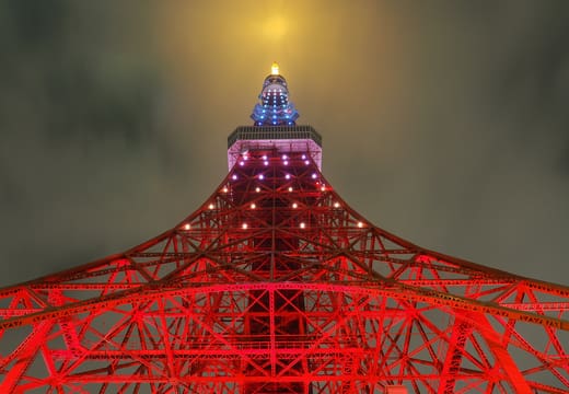 Looking up the glowing orange legs of Tokyo Tower into a hazy night sky