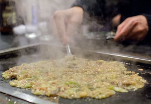 Monjayaki being mixed and cooked on a hot iron griddle in a Tsukishima restaurant