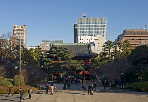 Stone approach to the red Sangedatsumon gate of Zojo-ji with office towers behind