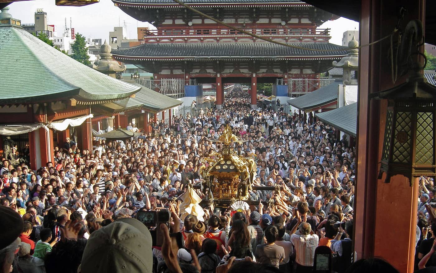 Dense crowds around a main mikoshi in the Senso-ji grounds, seen from the temple