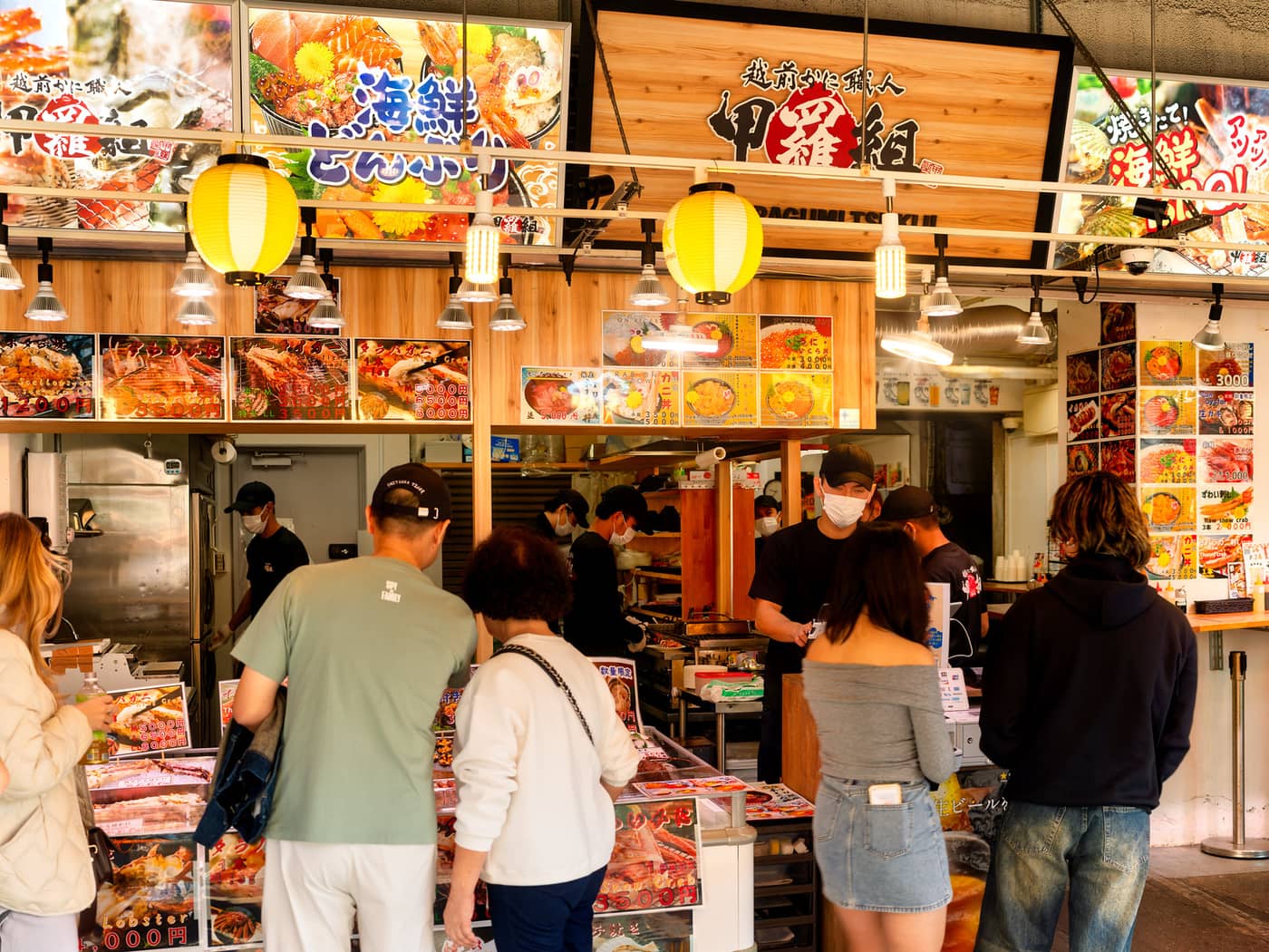 築地場外市場の店先で、赤い提灯の下で海鮮を注文する客たち