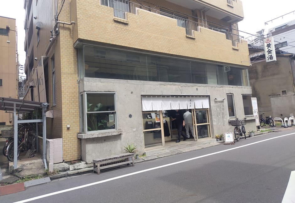 Concrete front and white noren of Koganeyu sento under an apartment block near Kinshicho