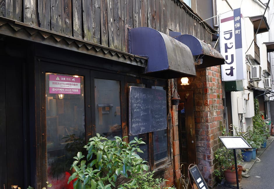 The dark timber front of Ladrio on a Jimbocho back lane, with its blue awning and vertical name sign