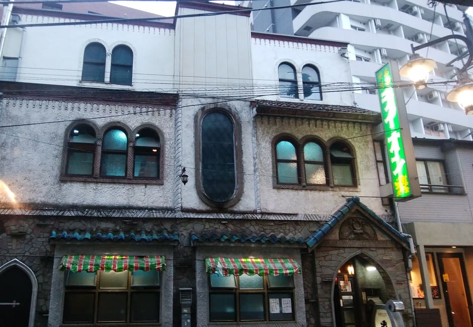 The stone-faced front of Meikyoku Kissa Lion on Dogenzaka, with arched windows and its green neon sign