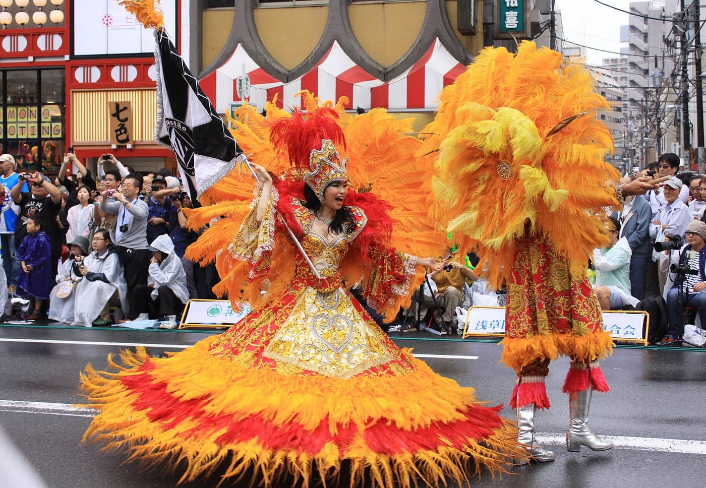 A samba dancer in an orange feathered costume parading through Asakusa at the carnival