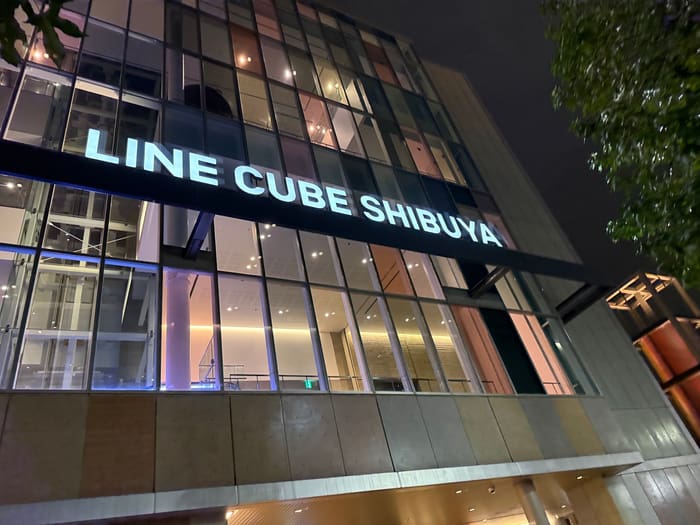 LINE CUBE SHIBUYA lettering across the lit glass front of the hall at night