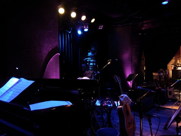 Stage of Minami-Aoyama Mandala set with piano and guitars under purple light