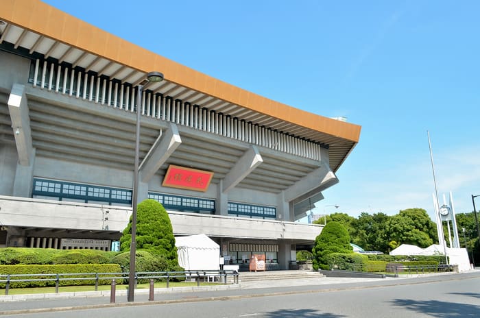 The Nippon Budokan's sweeping roof and facade in Kitanomaru Park under a blue sky