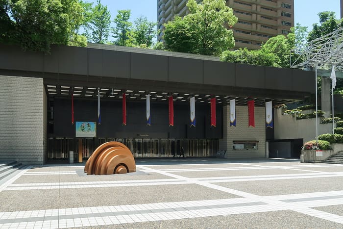 The entrance of Suntory Hall in Akasaka, seen across the paved plaza with its bronze sculpture