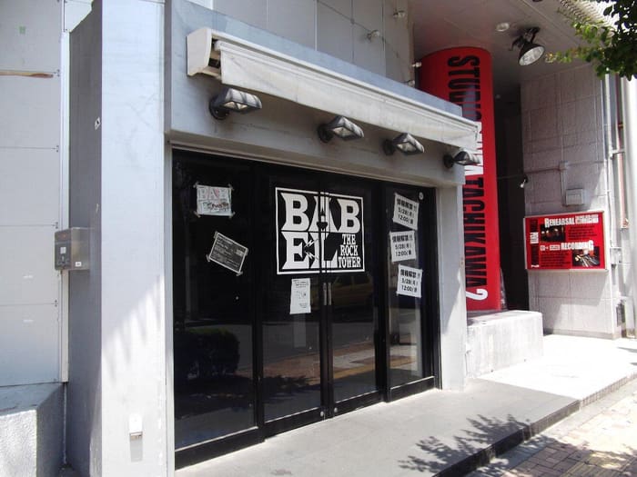 Black entrance doors and BABEL logo of the Tachikawa live house on a sunny street
